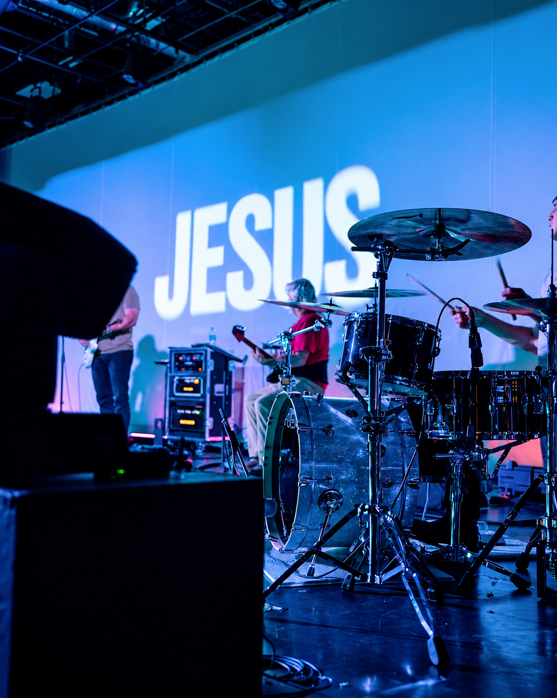 Worship band and drum kit on stage in blue light with JESUS projected on the backdrop